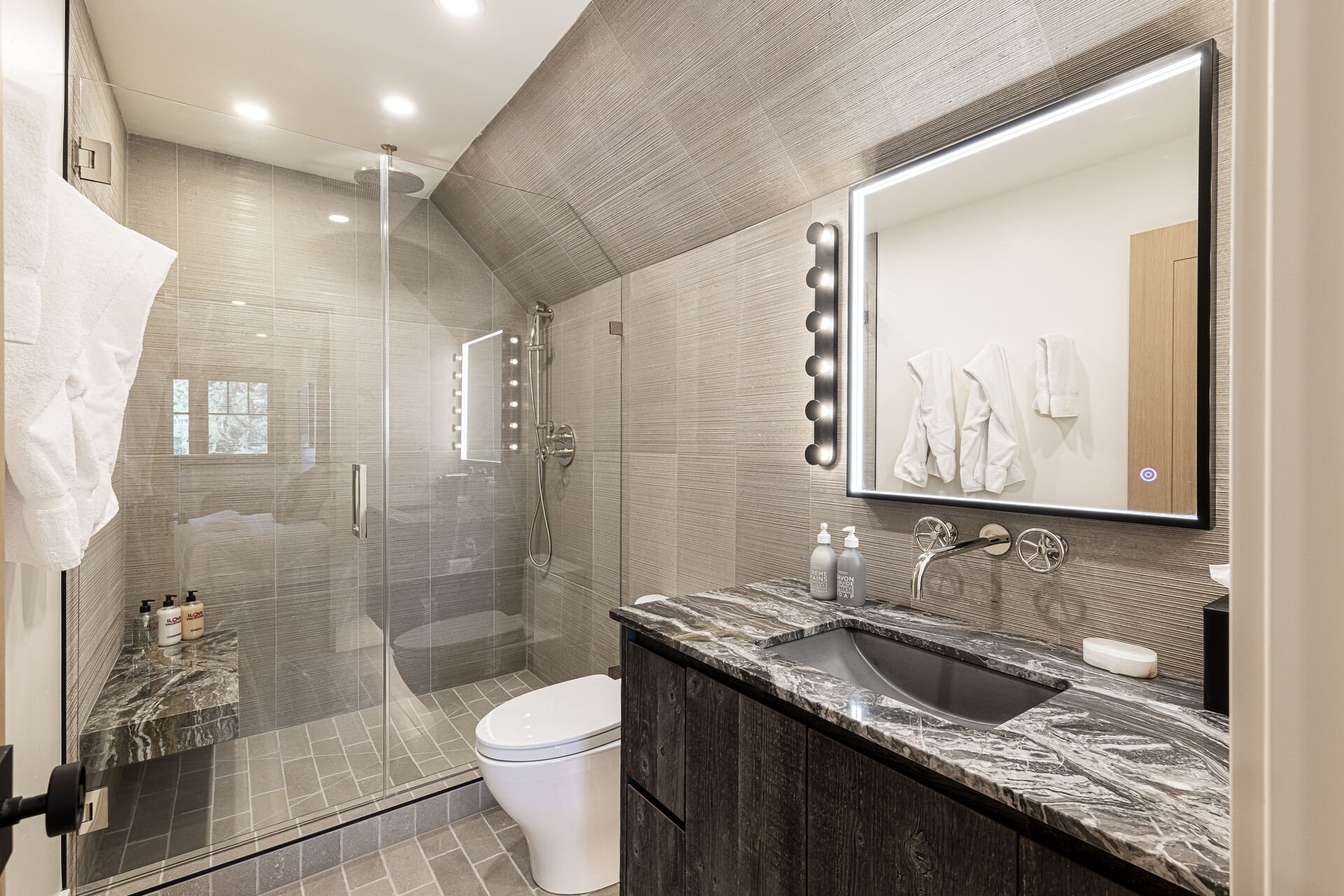 Sun Peak Manor House - Guest Bedroom 5 en suite stone counter vanity with lighted mirror and shower with a stone bench